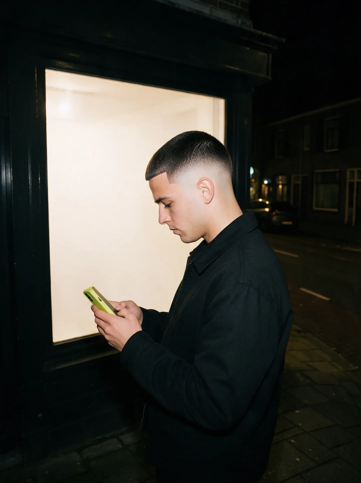 Een klant kijkt 's avonds op zijn telefoon voor een barbershop.