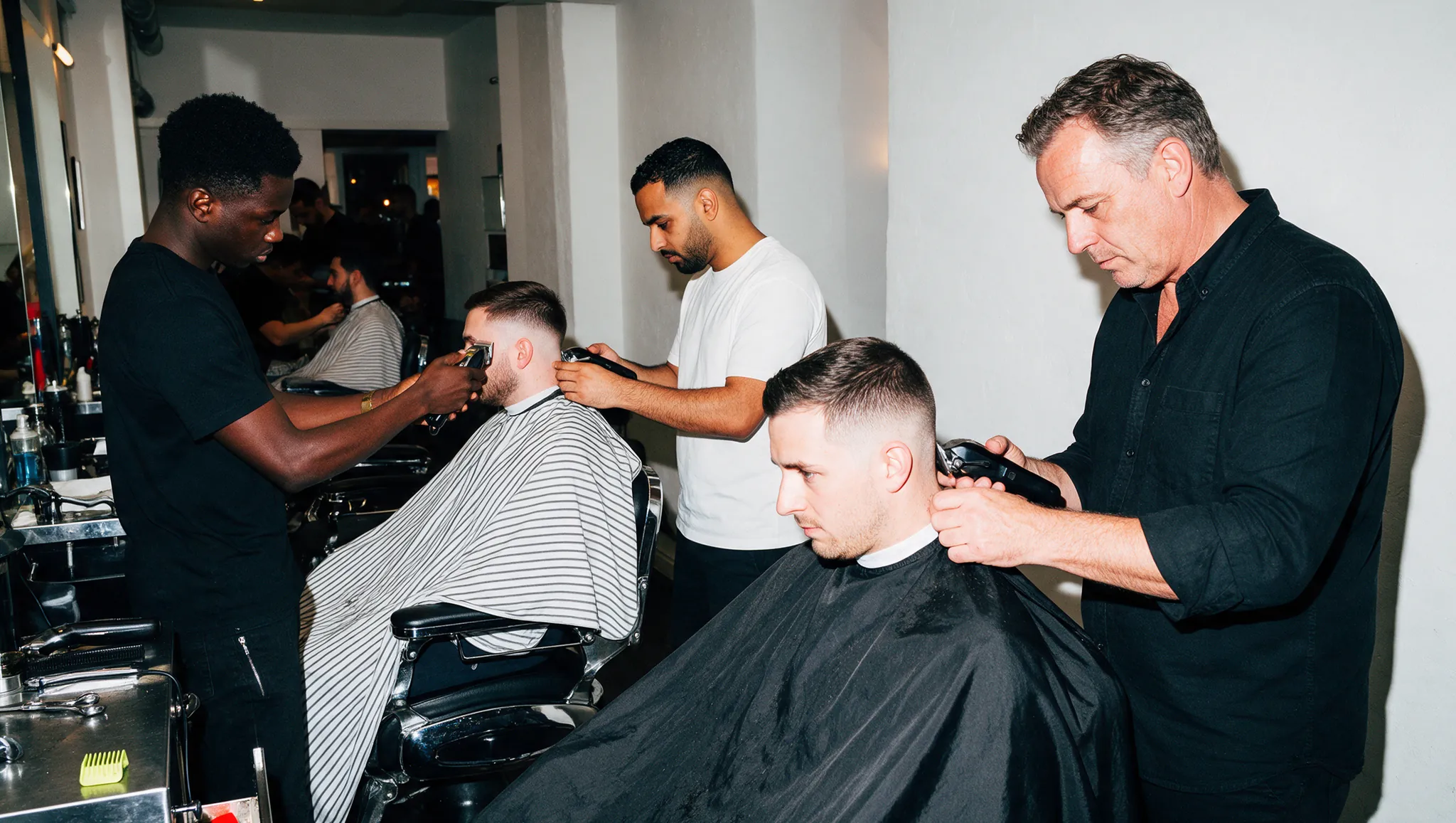 Drie barbers aan het werk in een volle zaak.